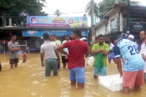People stand in knee-deep water on a flooded street in Sri Lanka as rescue efforts continue following Cyclone Ditwah.