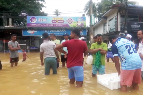 People stand in knee-deep water on a flooded street in Sri Lanka as rescue efforts continue following Cyclone Ditwah.
