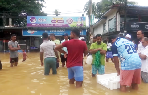 People stand in knee-deep water on a flooded street in Sri Lanka as rescue efforts continue following Cyclone Ditwah.