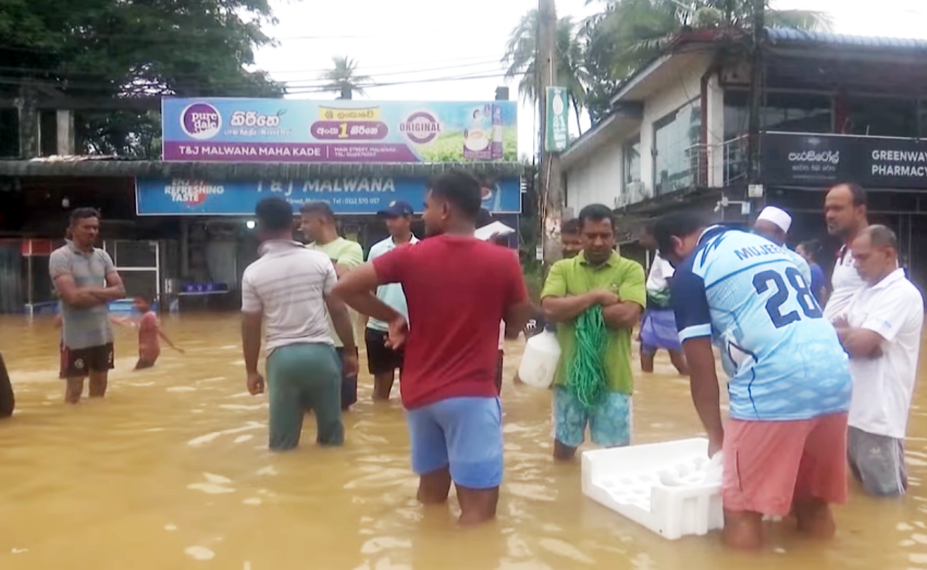People stand in knee-deep water on a flooded street in Sri Lanka as rescue efforts continue following Cyclone Ditwah.