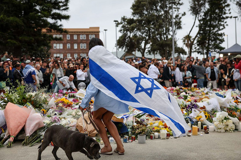 SYDNEY, AUSTRALIA - DECEMBER 15: A mourner wearing an Israeli flag lays flowers at Bondi Beach on December 15, 2025 in Sydney, Australia.