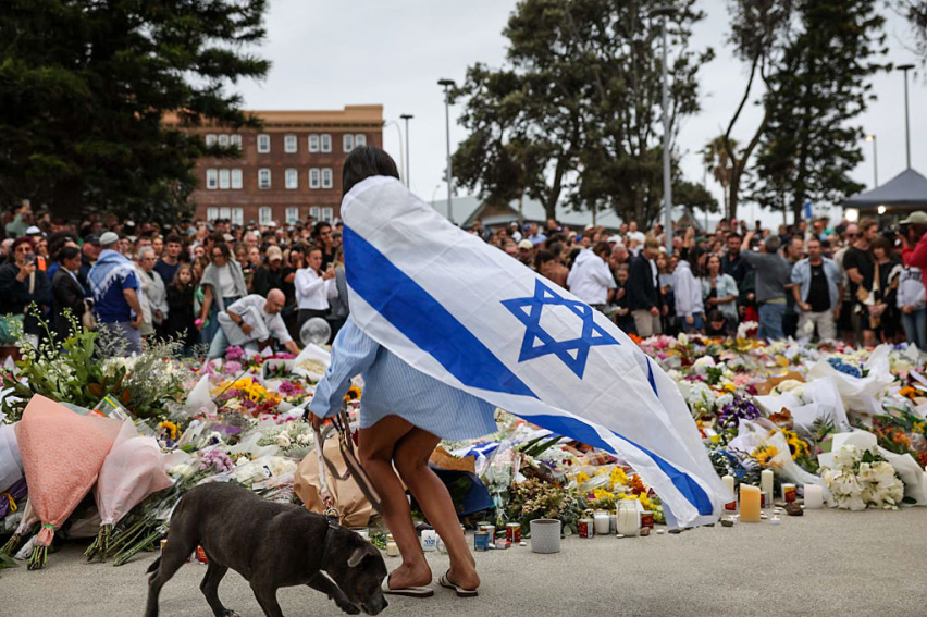 SYDNEY, AUSTRALIA - DECEMBER 15: A mourner wearing an Israeli flag lays flowers at Bondi Beach on December 15, 2025 in Sydney, Australia.