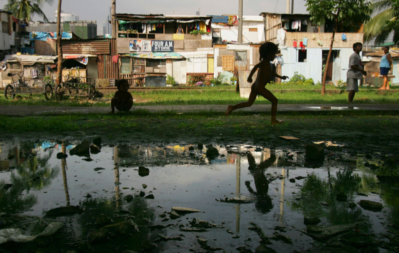 A boy runs near a mud puddle along the railroad tracks where hundreds of poverty stricken live in the slums in a Southeast Asian country.