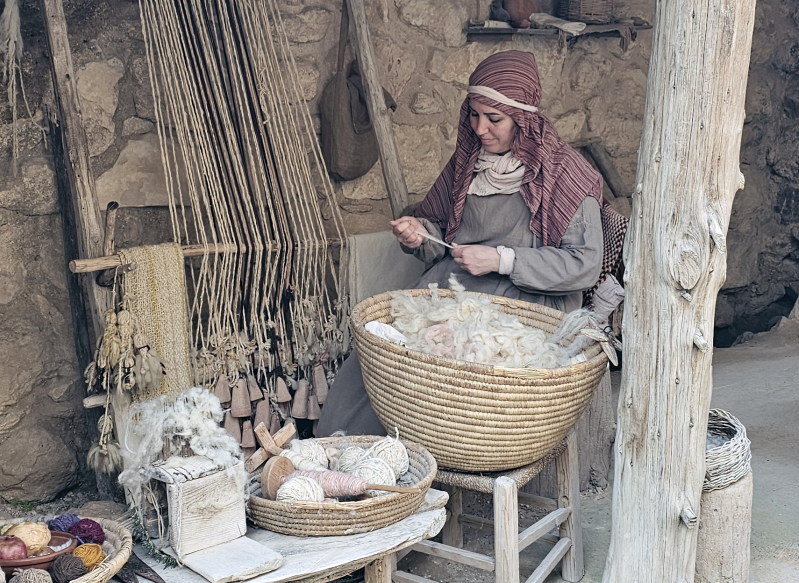 A woman portrayed in first-century dress works wool by hand at Nazareth Village, demonstrating textile skills used to produce clothing and household fabrics in Galilee during the time of Jesus.